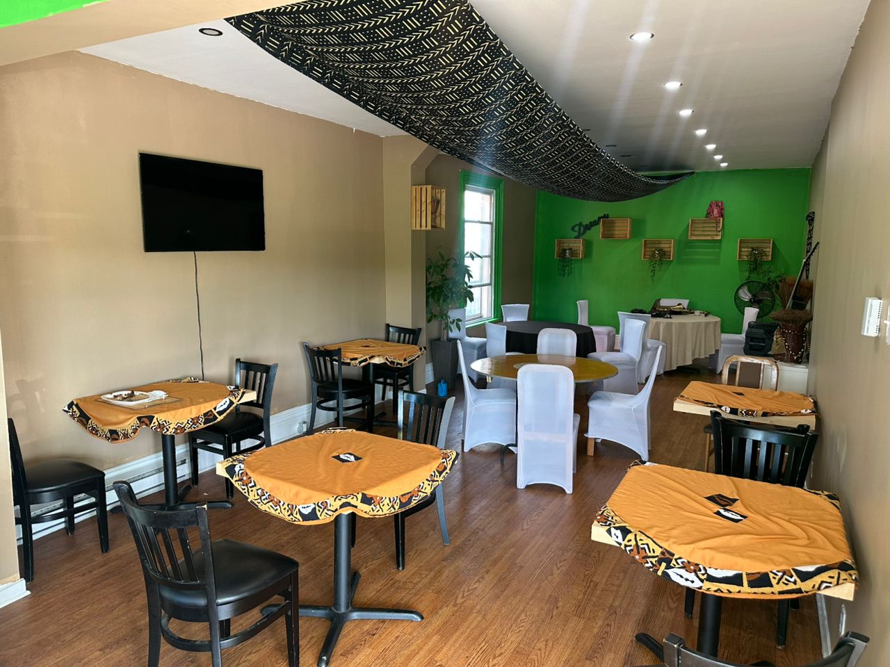 Tables nappées de pagne africain, chaises noires et téléviseur mural